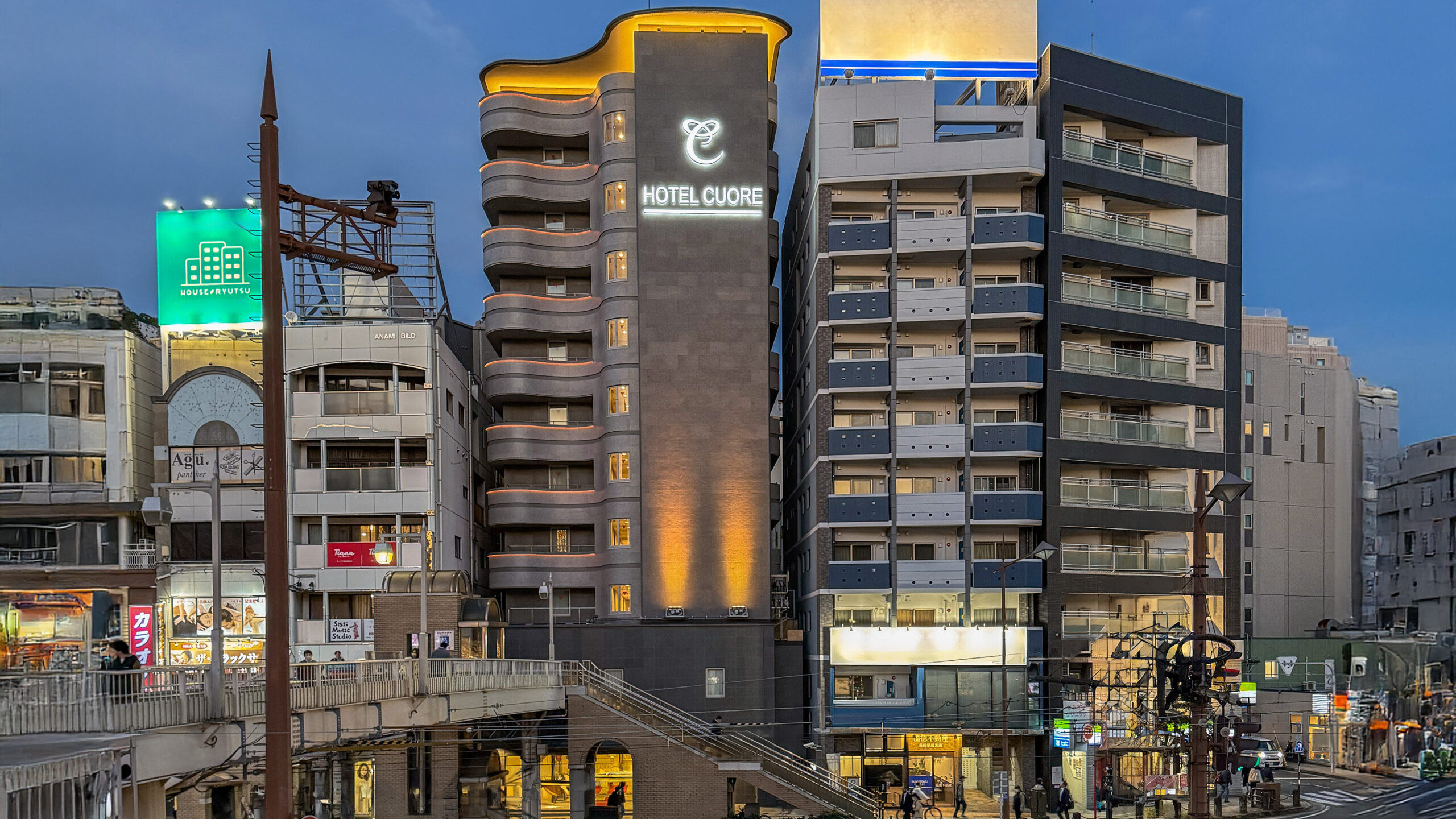 ホテル クオーレ長崎駅前の外観。夕暮れの空の下で、宿の名前が白く光っている